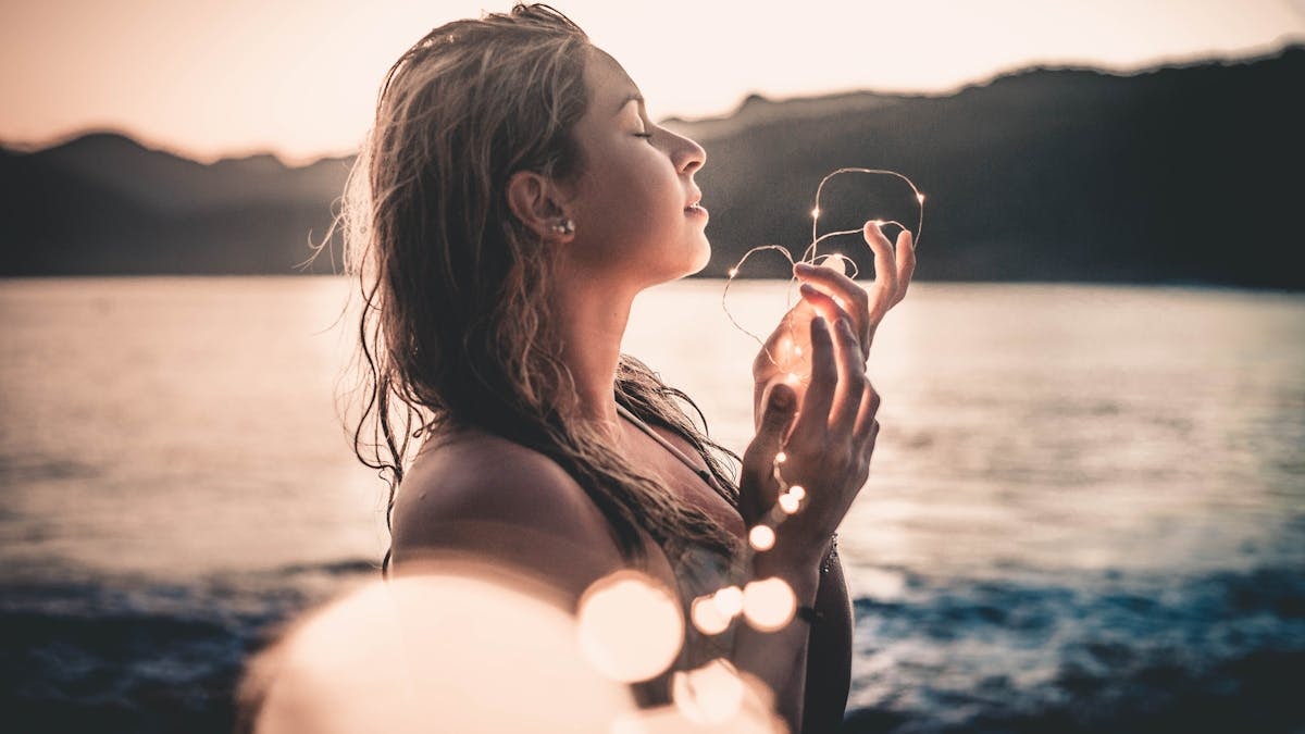 A woman enjoys a serene sunset on a beach in Ubatuba, Brazil holding glowing lights.